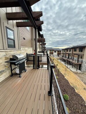 A wooden deck with a grill, a stone wall, and a view of a row of similar buildings. - 3-Bedroom Townhouse with Mountain and Lake Views. Sleep 9 (Heber City)