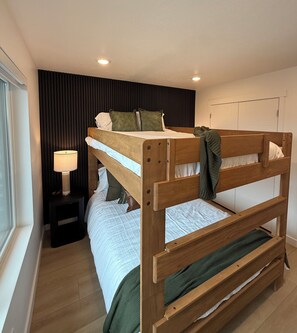 Ein Stockbett mit Holzrahmen, ein Nachttisch mit Lampe und ein Fenster mit Jalousien.