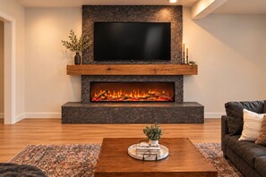 A modern living room with a stone fireplace, a flat-screen TV mounted above it, and a wooden coffee table with decorative items. - 3-Bedroom Townhouse with Mountain and Lake Views. Sleep 9 (Heber City)