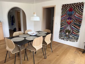 Una zona de menjador amb una taula rodona, quatre cadires, una làmpada penjant blanca i una catifa de paret multicolor.