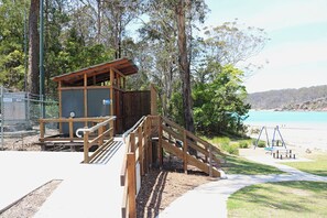 Eine Holzkonstruktion mit einer Rampe, die zu einem Strandabschnitt führt, umgeben von Bäumen und einem Zaun.