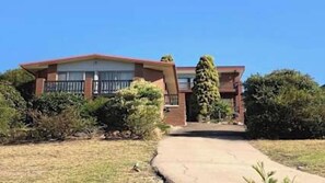 A two-story house with a front porch, a small garden, and a clear sky. - Suncrest Apartment - Pambula Beach (Pambula Beach)