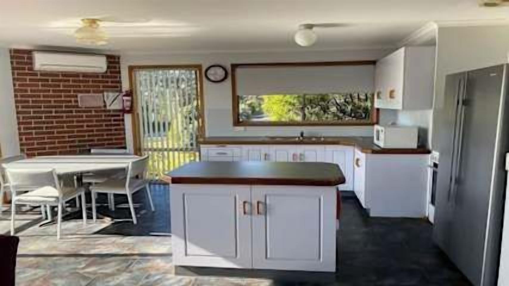 Cocina compacta con isla central, muebles blancos y ventana que proporciona luz natural.
