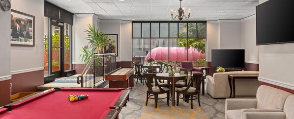 A billiards table, multiple chairs, a sofa, a television, and a large window with a view.
