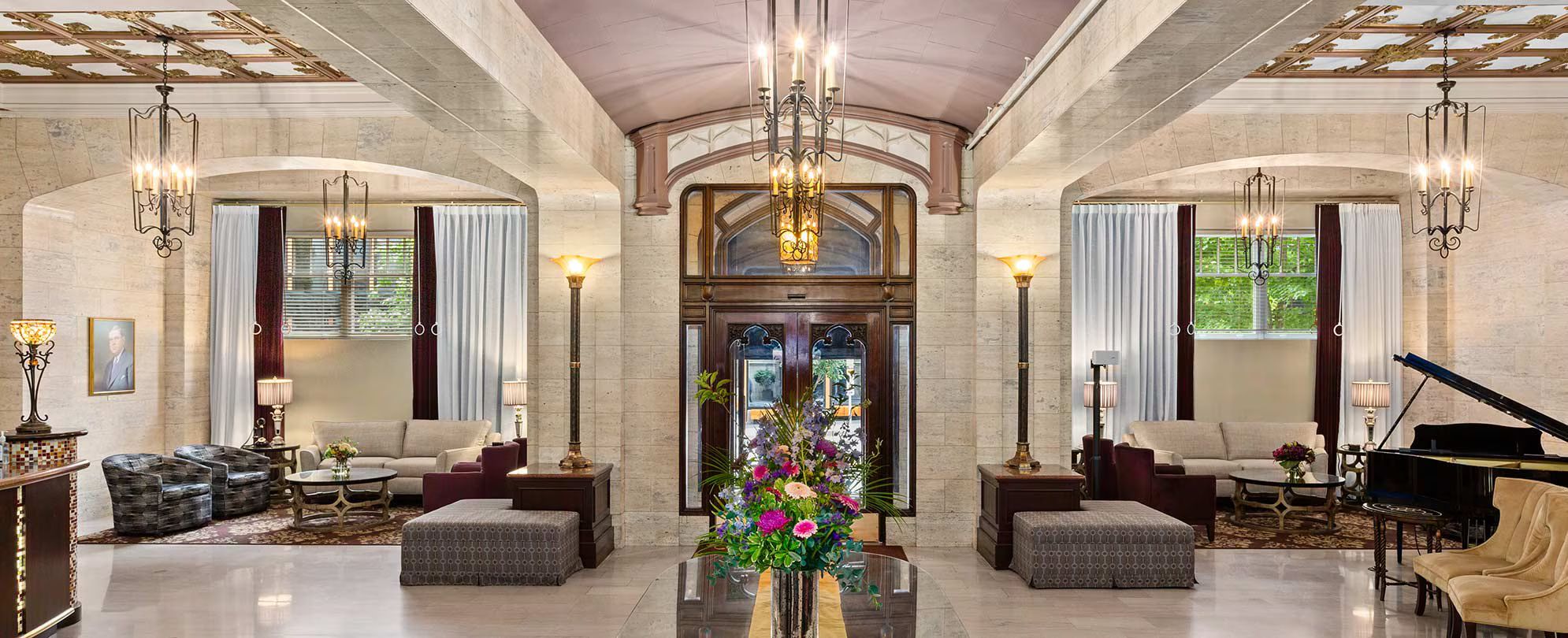 A grand lobby with a grand piano, elegant chandeliers, and a central floral arrangement.