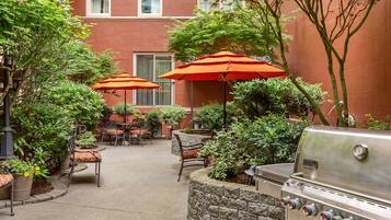 An outdoor patio area with stone seating, orange umbrellas, and a built-in barbecue grill.