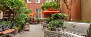 Eine Außenpatio-Terrasse mit Steinsitzgelegenheiten, orangefarbenen Sonnenschirmen und einem integrierten Grill.