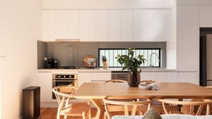 A modern kitchen with white cabinets, a wooden dining table, and chairs. - Cuthbert Place Broadmeadows (Broadmeadows)