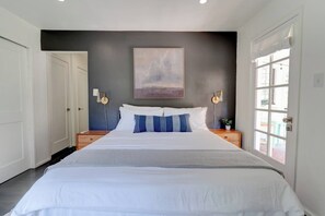A bedroom with a large bed, two bedside tables, a wall-mounted lamp, and a window with curtains. - Nature Lovers Casita! King Bed! Big Backyard (Fresno)