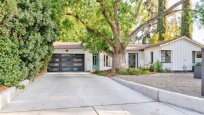 A residential driveway leading to a garage with a white house and a tree in the foreground.