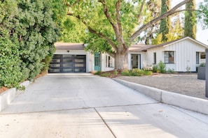 A residential driveway leading to a garage with a white house and a tree in the foreground.