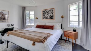 A bedroom with a large bed, bedside tables, a desk, and a window with curtains.