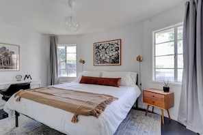 A bedroom with a large bed, bedside tables, a desk, and a window with curtains.