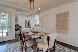 A dining area with a table set for four, a chandelier, and a macrame wall hanging. - Nature Lovers Casita! King Bed! Big Backyard (Fresno)