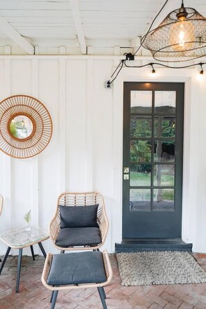 A room with a dark door, wicker furniture, a glass table, and a hanging light fixture. - Nature Lovers Casita! King Bed! Big Backyard (Fresno)