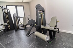 Une salle de sport équipée de divers appareils d’exercice, d’un banc et d’une fenêtre.