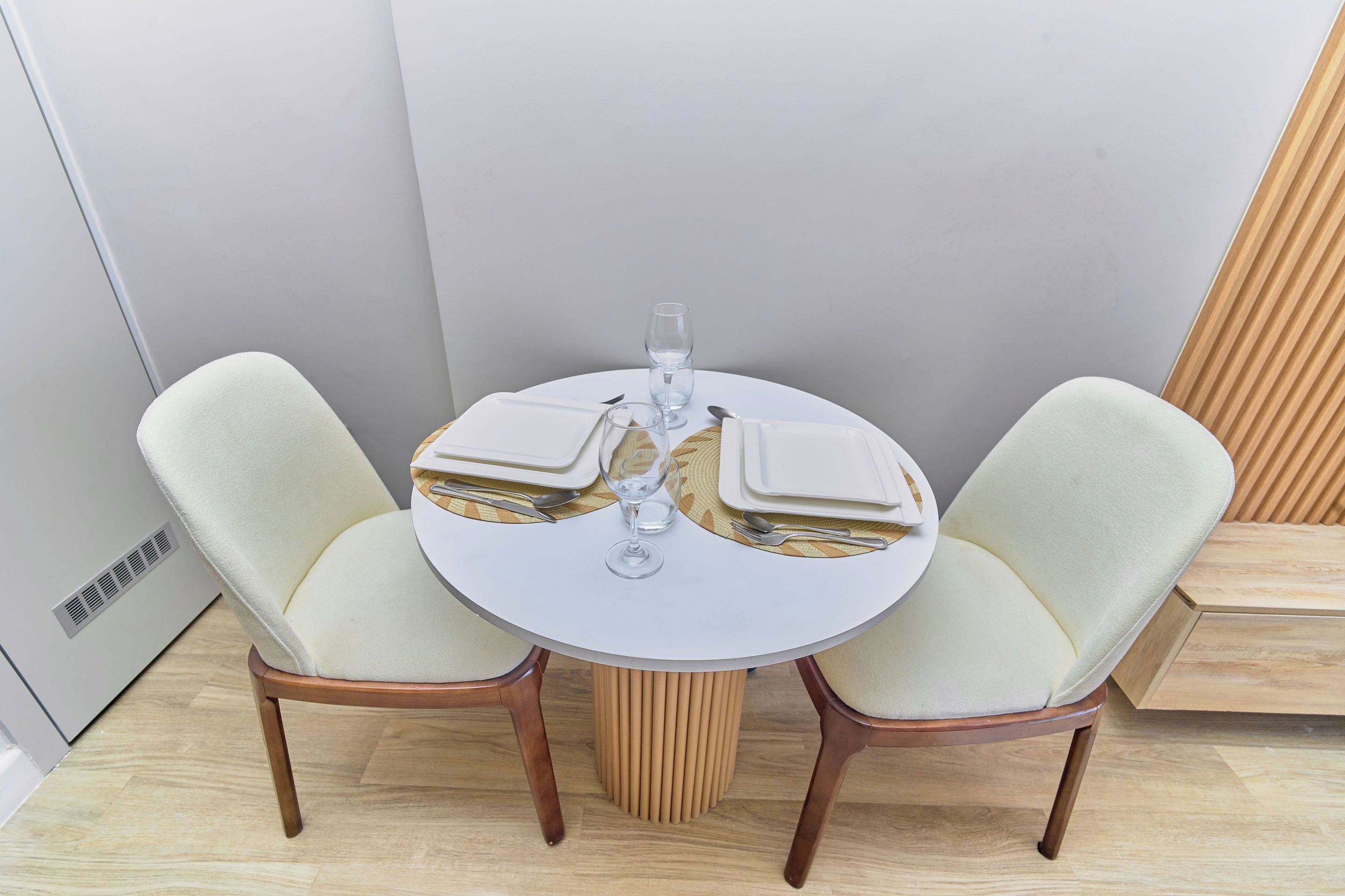 A round dining table with two chairs, a glass of water, and cutlery.