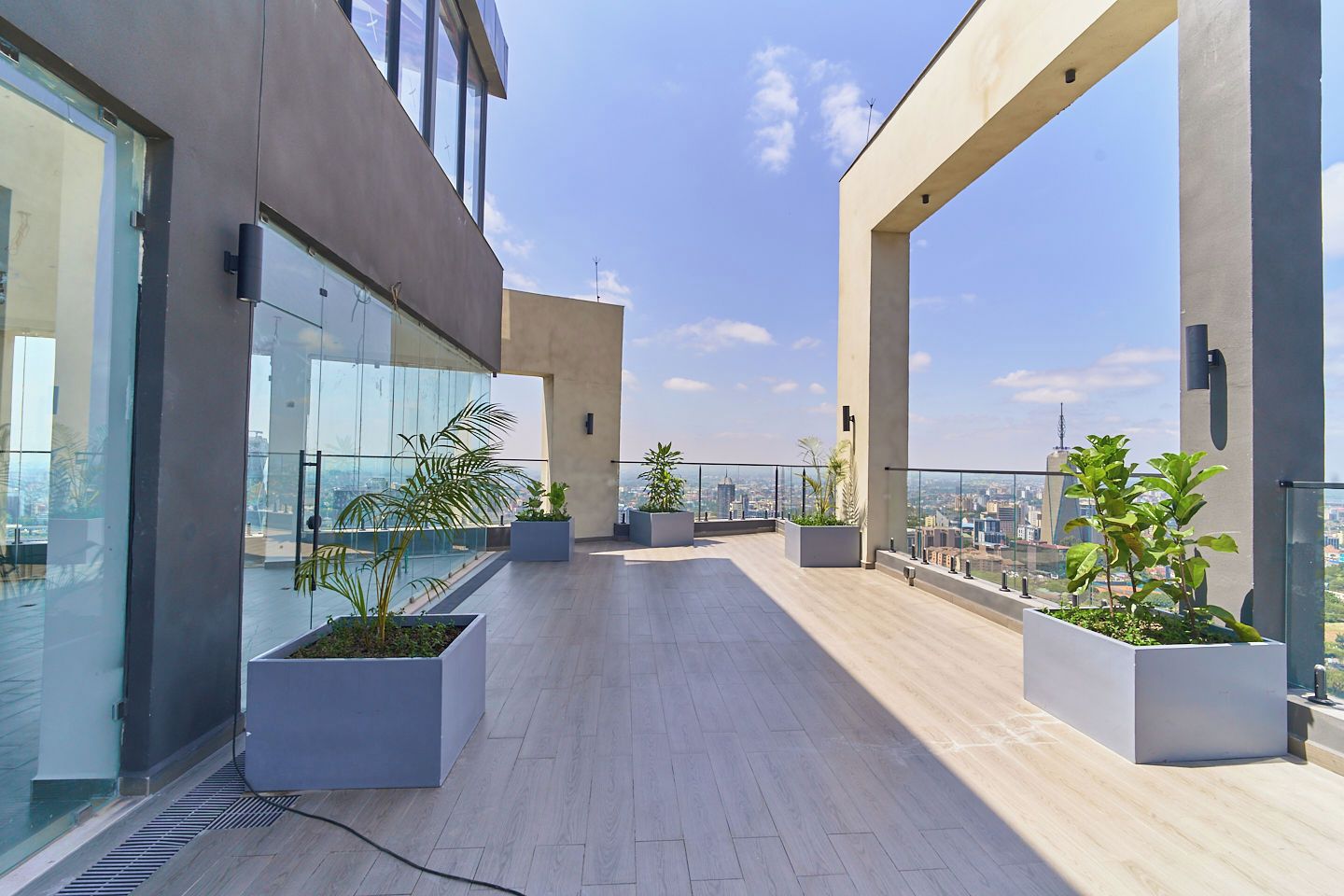 Eine Dachterrasse mit großen Fenstern, Topfpflanzen und Blick auf die Stadt.