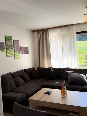 Una sala de estar con un sofá seccional, una mesa de centro de madera y vista a un paisaje verde por la ventana.