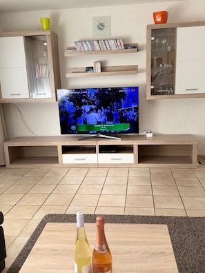A living room with a flat-screen TV, wooden cabinets, and a coffee table with bottles. - A Natural Paradise in Herrenschwand. (Todtnau)