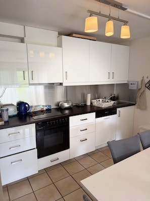 A modern kitchen with white cabinets, a black stove, and a dining area with a table and chairs. - A Natural Paradise in Herrenschwand. (Todtnau)