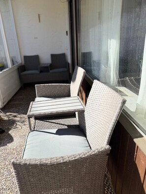 Un espacio de estar exterior con muebles de mimbre, una mesa, sillas, una ventana y un sofá al fondo.
