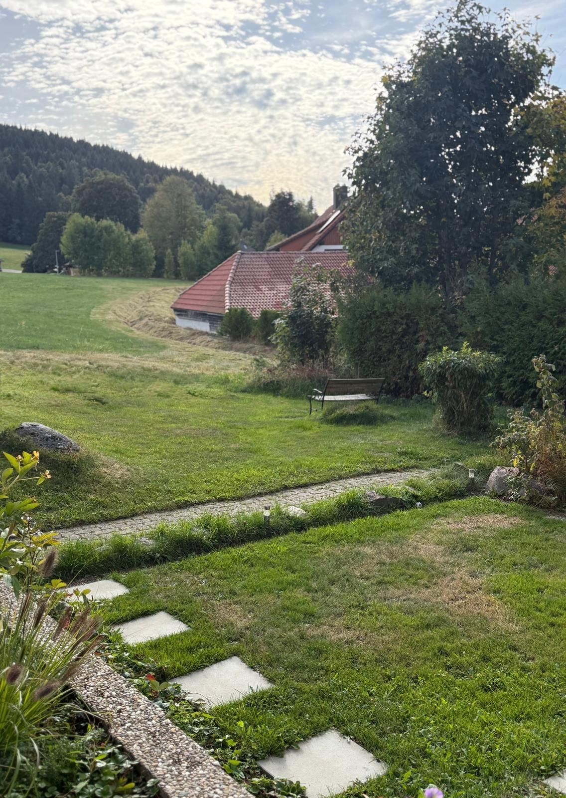 A rural landscape with a house, a stone pathway, and a grassy field.