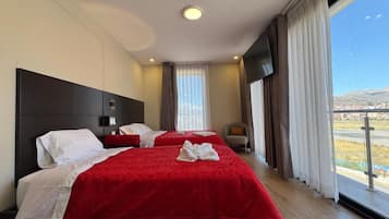 Una camera d'albergo con due letti, un'ampia finestra con tende, una TV a schermo piatto e vista sull'esterno.