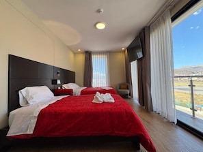 A hotel room with two beds, a large window with curtains, a flat-screen TV, and a view of the outdoors. - Hotel San Miguel Cusco (CUSCO)
