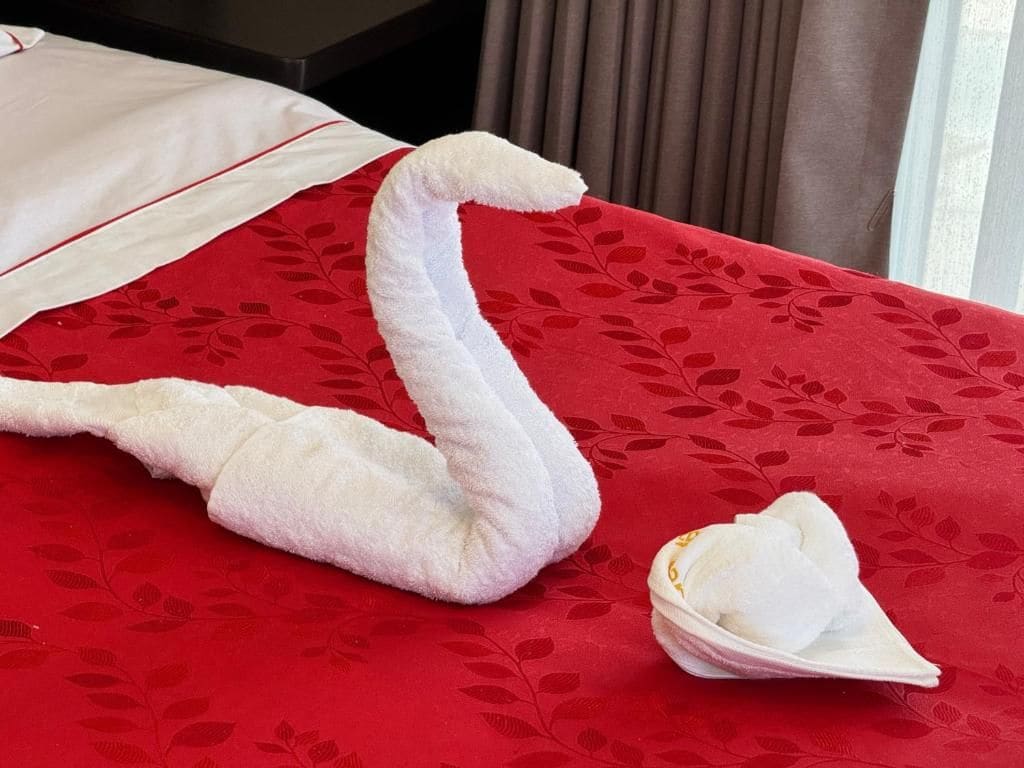 Een bed met een rode bedspreide met bloemen en een handdoek gevouwen in de vorm van een zwaan.