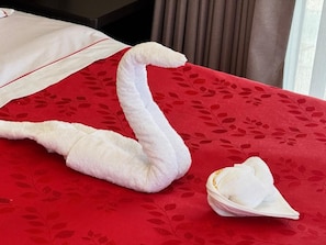 A bed with a red floral bedspread and a white towel shaped like a swan. - Hotel San Miguel Cusco (CUSCO)