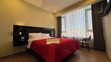Quarto de hotel com uma cama grande, televisão de tela plana, mesa pequena e uma cadeira.