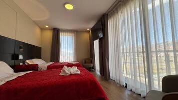 A hotel room with two beds, a TV, and large windows with curtains.
