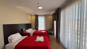 Quarto de hotel com duas camas, televisão de tela plana e uma janela grande com cortinas.