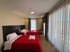 Habitació d'hotel amb dos llits, una televisió de pantalla plana i una finestra gran amb cortines.