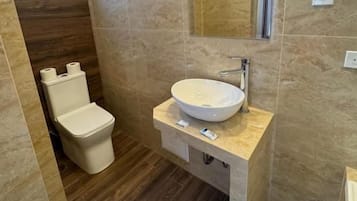 Un baño moderno con pared de mármol, un lavabo redondo y un inodoro.