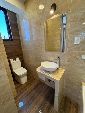 Bany modern amb paret de marbre, un lavabo rodó i un vàter.