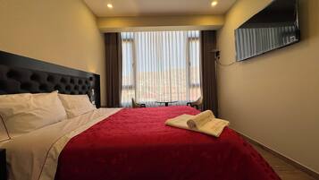 Een hotelkamer met een groot bed, een flatscreen televisie aan de muur en uitzicht op de stad door het raam.