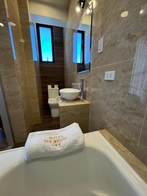 A bathroom with a bathtub, a sink, and a toilet. A towel with 'HOTEL SAN MIGUEL' is placed on the bathtub. - Hotel San Miguel Cusco (CUSCO)