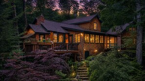 A large wooden house with multiple levels, a balcony, and a staircase leading to the entrance.