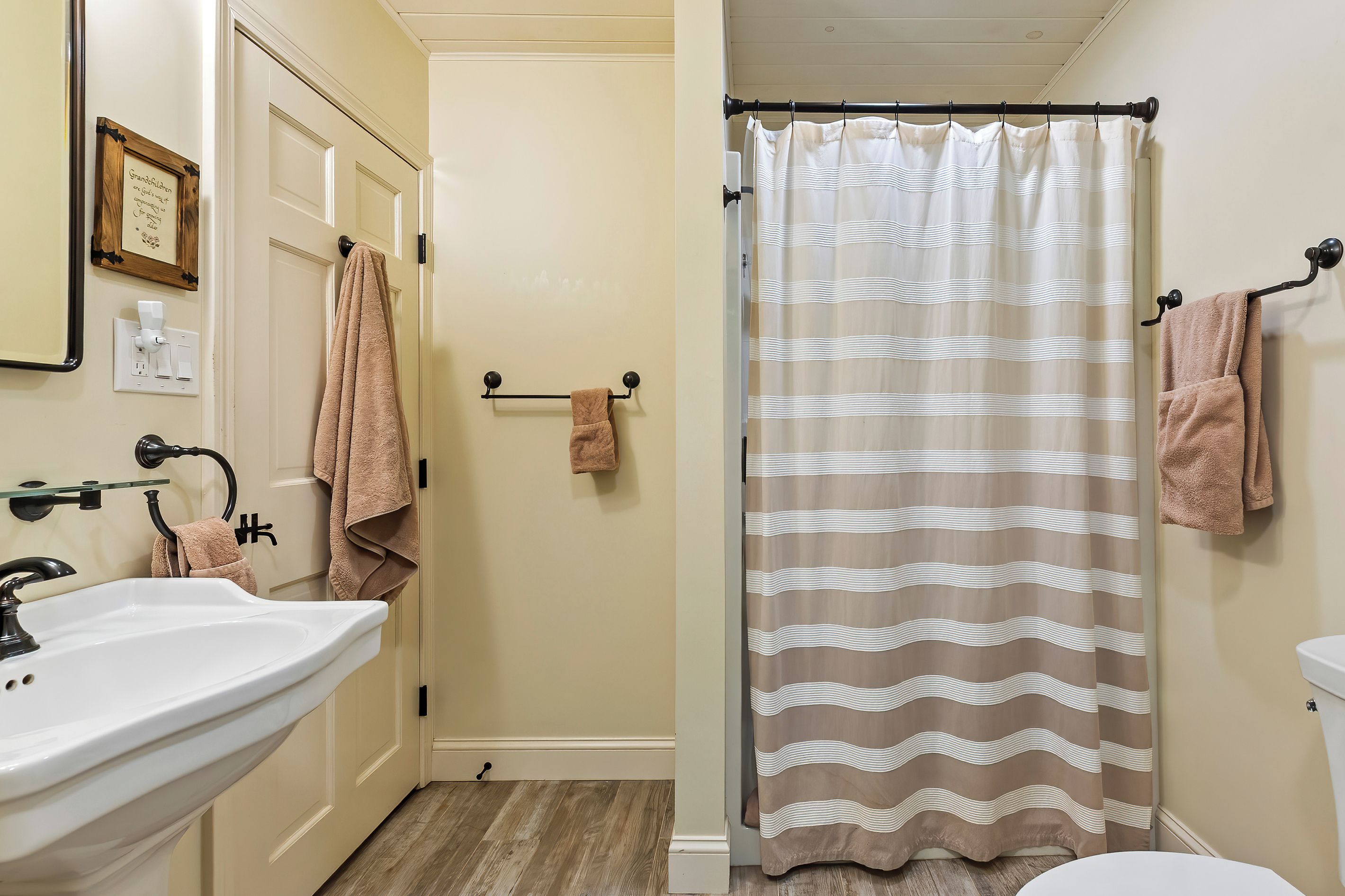 A bathroom with a white sink, a beige toilet, a shower curtain with a wavy pattern, and two towels hanging on hooks.