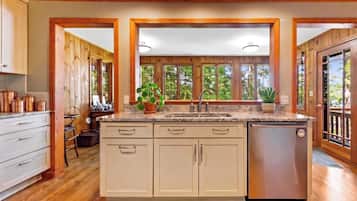 A kitchen with wooden cabinets, a stainless steel dishwasher, and a window with a view of trees.
