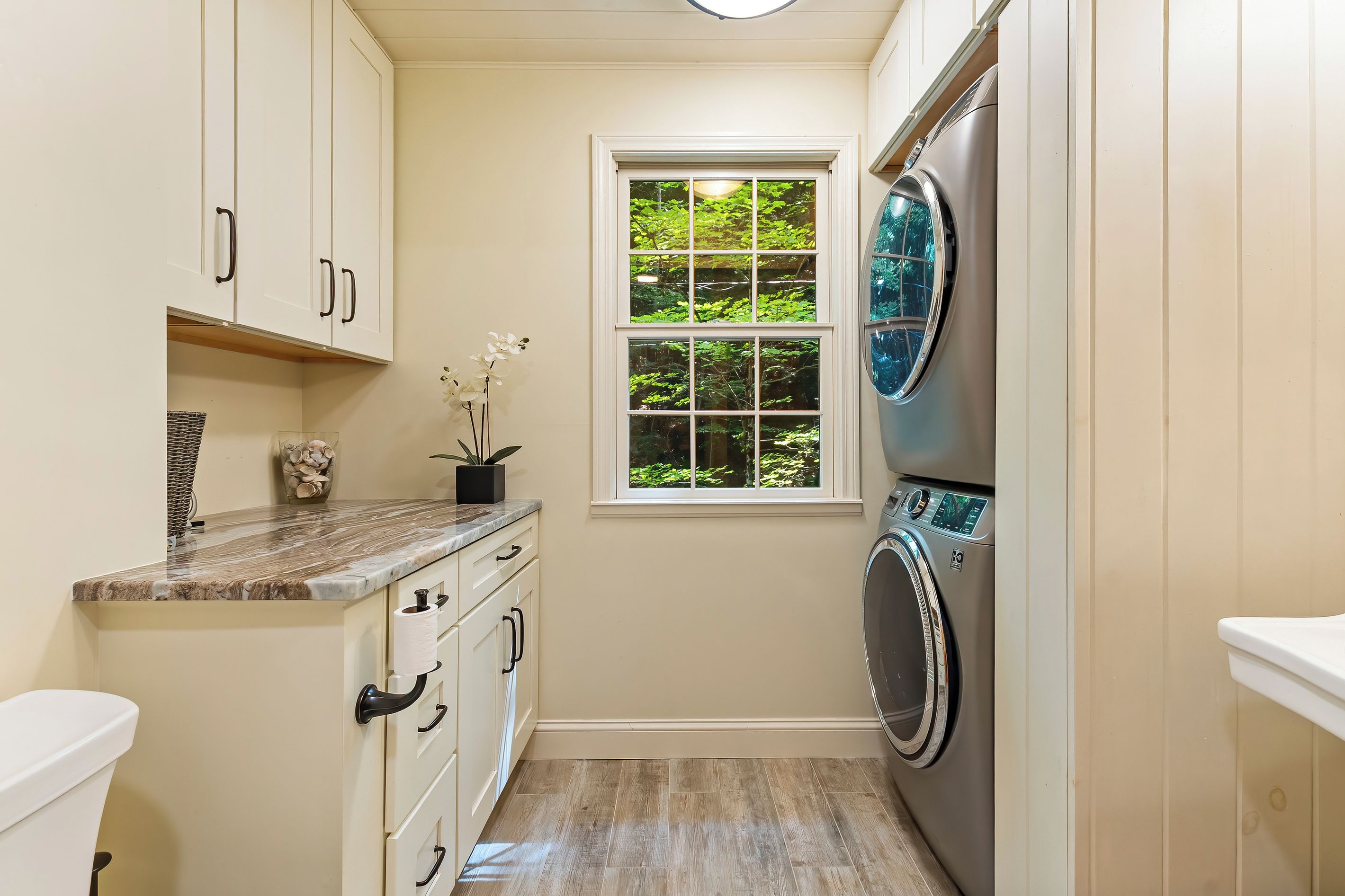 A compact laundry room with a washing machine, a small window with a view of greenery, and a marble countertop.