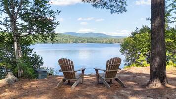 Two Adirondack chairs facing a lake with mountains in the background.
