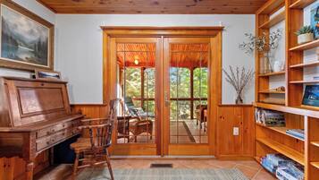A wooden interior with a piano, chairs, a bookshelf, and a view through a glass door.