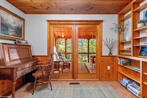 A wooden interior with a piano, chairs, a bookshelf, and a view through a glass door.