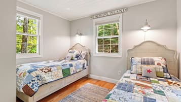 A bedroom with two beds, a wooden headboard, a quilted bedspread, and a view of trees through the windows.