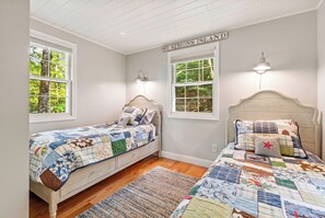 A bedroom with two beds, a wooden headboard, a quilted bedspread, and a view of trees through the windows. - Private Lake Beach & Dock | 20 Min to Ragged Mtn and Mt. Sunapee | Sleeps 6 (Sutton)