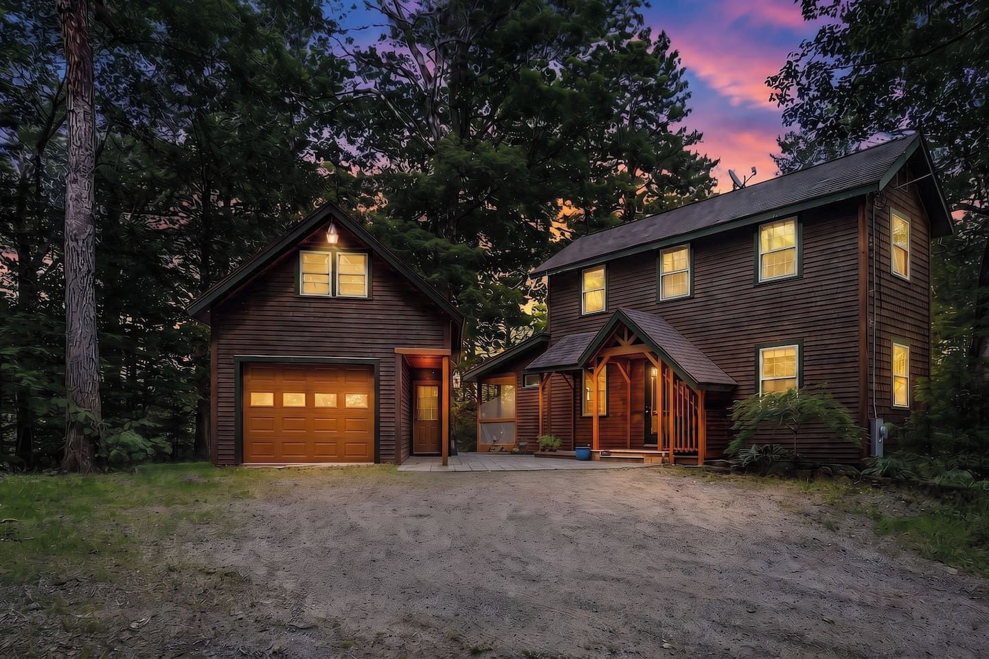 Ein zweigeschossiges Holzhaus mit Garage, umgeben von Bäumen und einer unbefestigten Auffahrt.