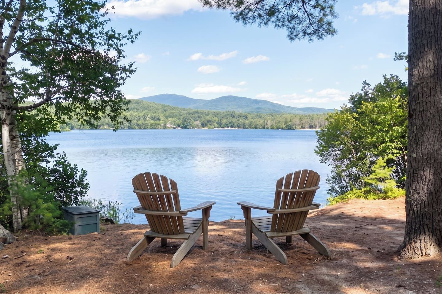 Dos sillas Adirondack mirando un lago con montañas al fondo.